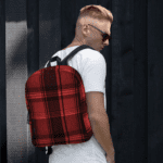 A man wearing a Backpack in Celtic Red Highland Plaid, can hold up to a 15" Laptop, or Tablet, many pockets for more, Padded Shoulder Strapssturdy, Water Resistant.