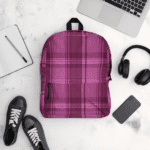 A Celtic Fucia Pink and Burgundy and Black Highland Plaid backpack with headphones and earphones on a white surface.