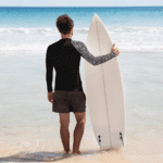 Man in black shirt holding surfboard on beach.