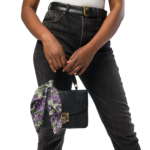 Woman in jeans holding a black bag with floral scarf.