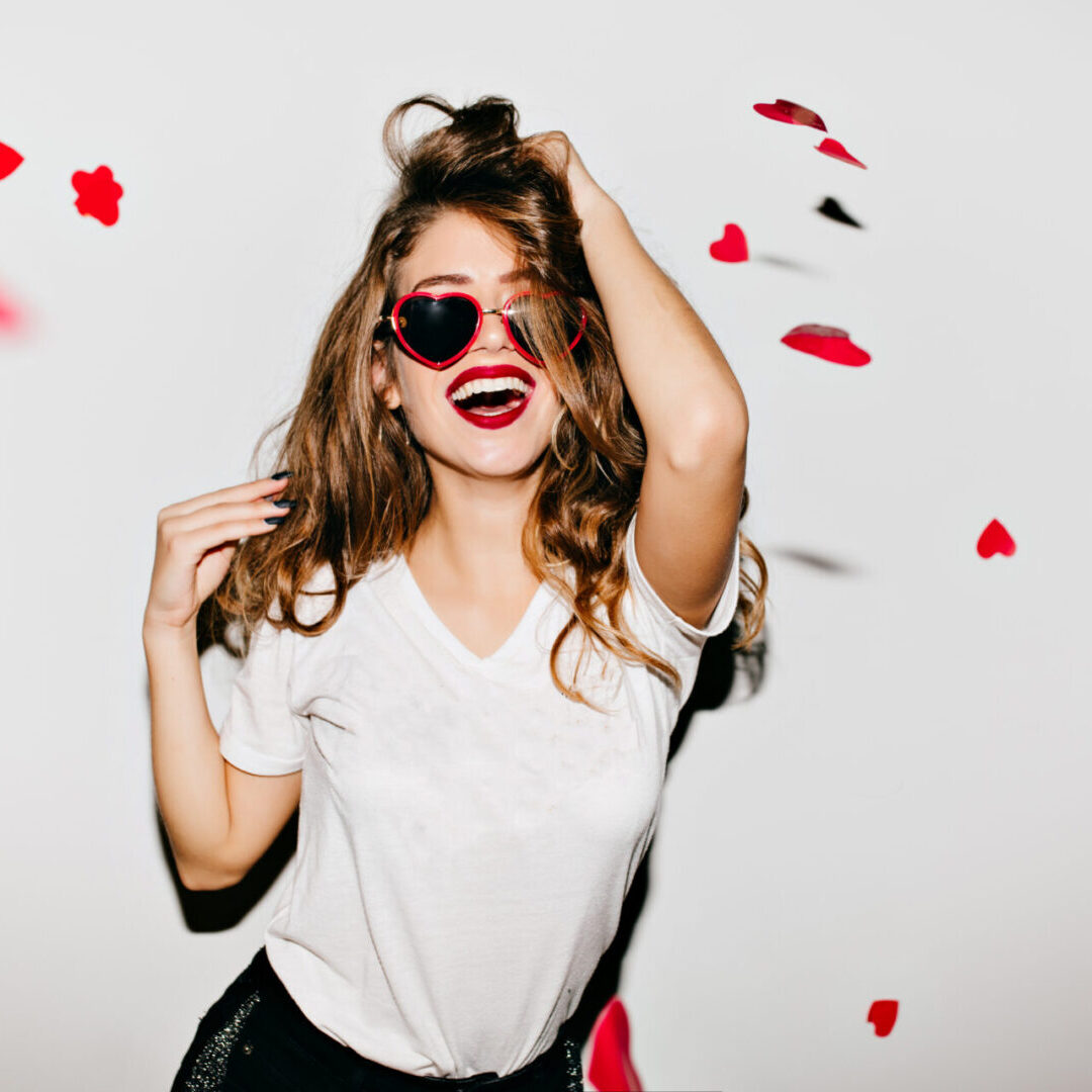 Woman with heart-shaped sunglasses smiles.